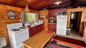 A wooden cabin interior with a kitchen area featuring a stove, sink, and refrigerator.