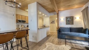 A modern kitchen with wooden cabinets, a dining area with bar stools, a gray sofa, and a fluffy rug. - Easy Access to Skiing!  Elevator, Hot Tub! (Mount Crested Butte)