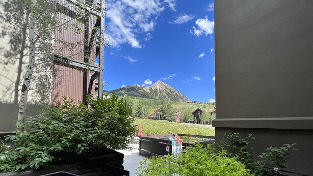A balcony with a wooden chair, a small pool, and a view of a mountain and houses in the distance. - Easy Access to Skiing!  Elevator, Hot Tub! (Mount Crested Butte)