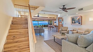 A spacious living area with a wooden staircase, a ceiling fan, and a view of the ocean. - Spectacular Oceanfront 4 bedroom 4 bath, AC, pool in tropical oasis. (Lahaina)