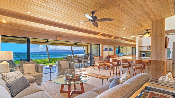 A spacious living area with a large sofa, coffee table, and dining area. A ceiling fan is visible, and the room has large windows offering a view of the ocean. - Spectacular Oceanfront 4 bedroom 4 bath, AC, pool in tropical oasis. (Lahaina)