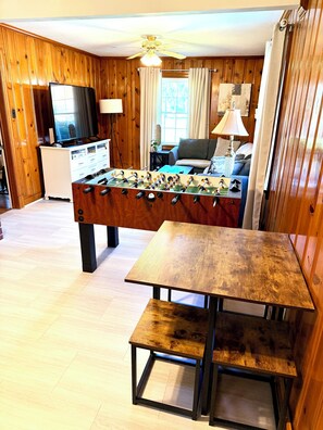 A room with a foosball table, a television, a sofa, and a dining table. - 3 bedroom cozy yet spacious home w/ in-ground pool (Richmond)