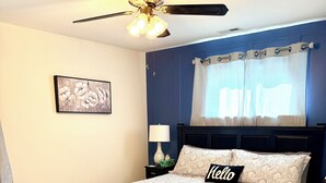 A bedroom with a bed, a ceiling fan, a nightstand, a lamp, a window with curtains, and a wall-mounted painting. - 3 bedroom cozy yet spacious home w/ in-ground pool (Richmond)