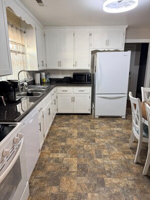 A kitchen with white cabinets, a black countertop, a white refrigerator, and a stone-patterned floor. - 3 bedroom cozy yet spacious home w/ in-ground pool (Richmond)