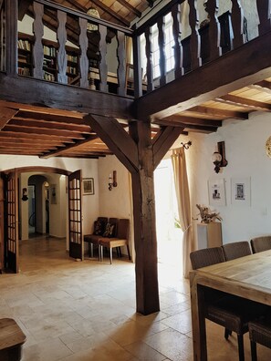 Una habitación amplia con techo alto, vigas de madera, una mesa grande y una zona de estar con sillas.