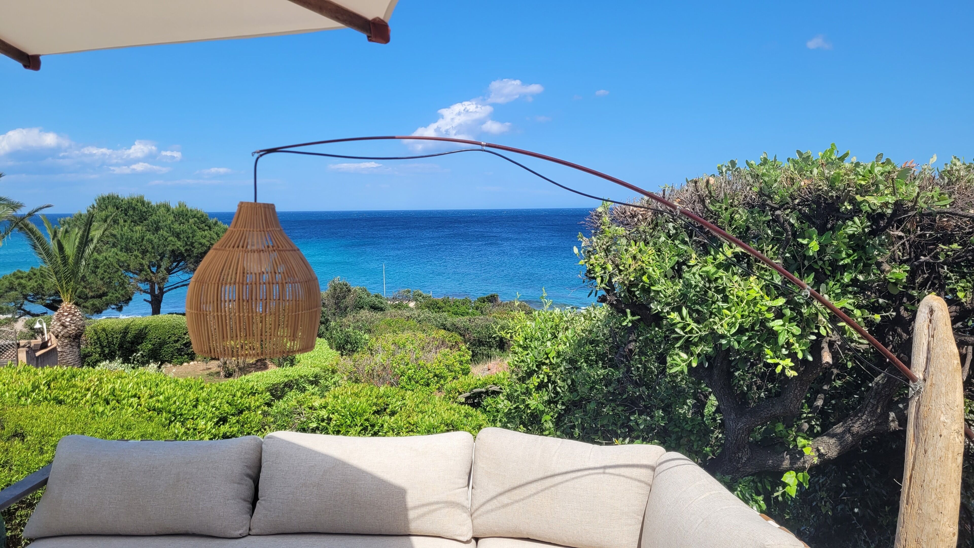 A coastal outdoor seating area with a hanging light fixture, a view of the sea, and lush greenery.
