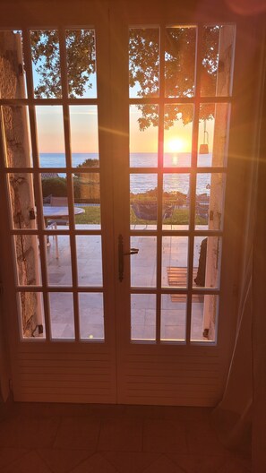 A door with multiple glass panels, leading to an outdoor patio area with a view of the sea and a sunset. -  Exclusive granite villa DIRECTLY on the beach, sea and mountain panorama, pool (Zonza)