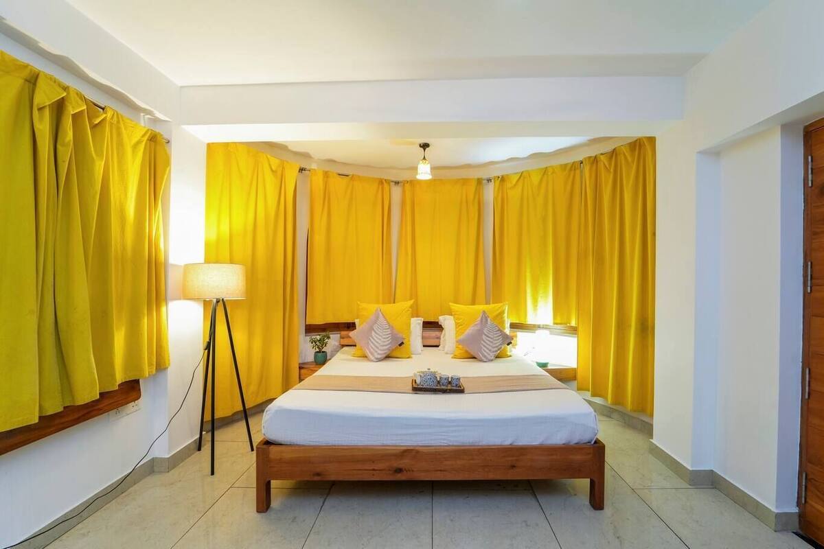 A bedroom with a wooden bed, yellow curtains, a bedside lamp, and a wooden door.