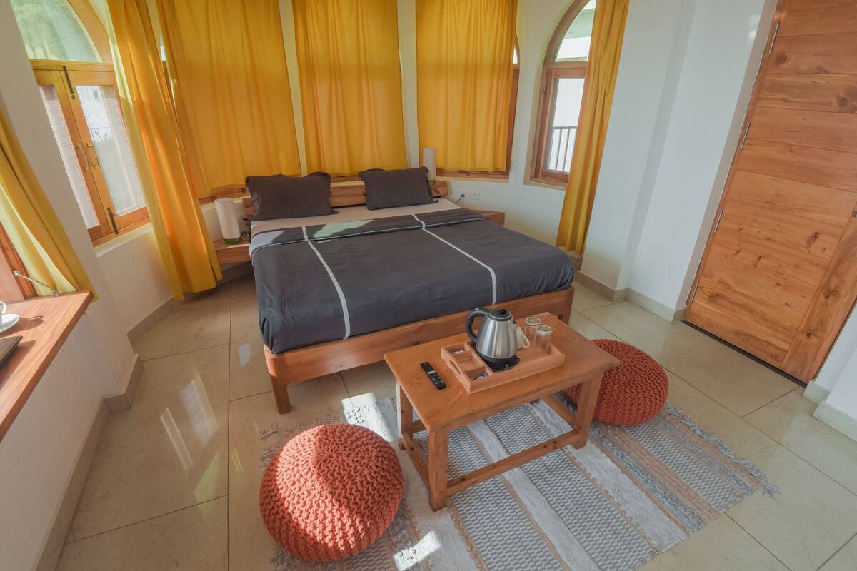 A bedroom with a bed, wooden bedside tables, a coffee table, and a window with curtains.