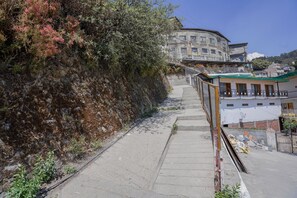 A narrow concrete pathway leading to a building with a curved facade, a small balcony, and a satellite dish. - Mussoorie Estate by Dumnu Homes (Dehradun)