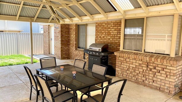 An outdoor patio with a brick barbecue grill, a glass table, and chairs.