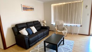 A living room with a black sofa, a small table, a chair, and a window with sheer curtains.