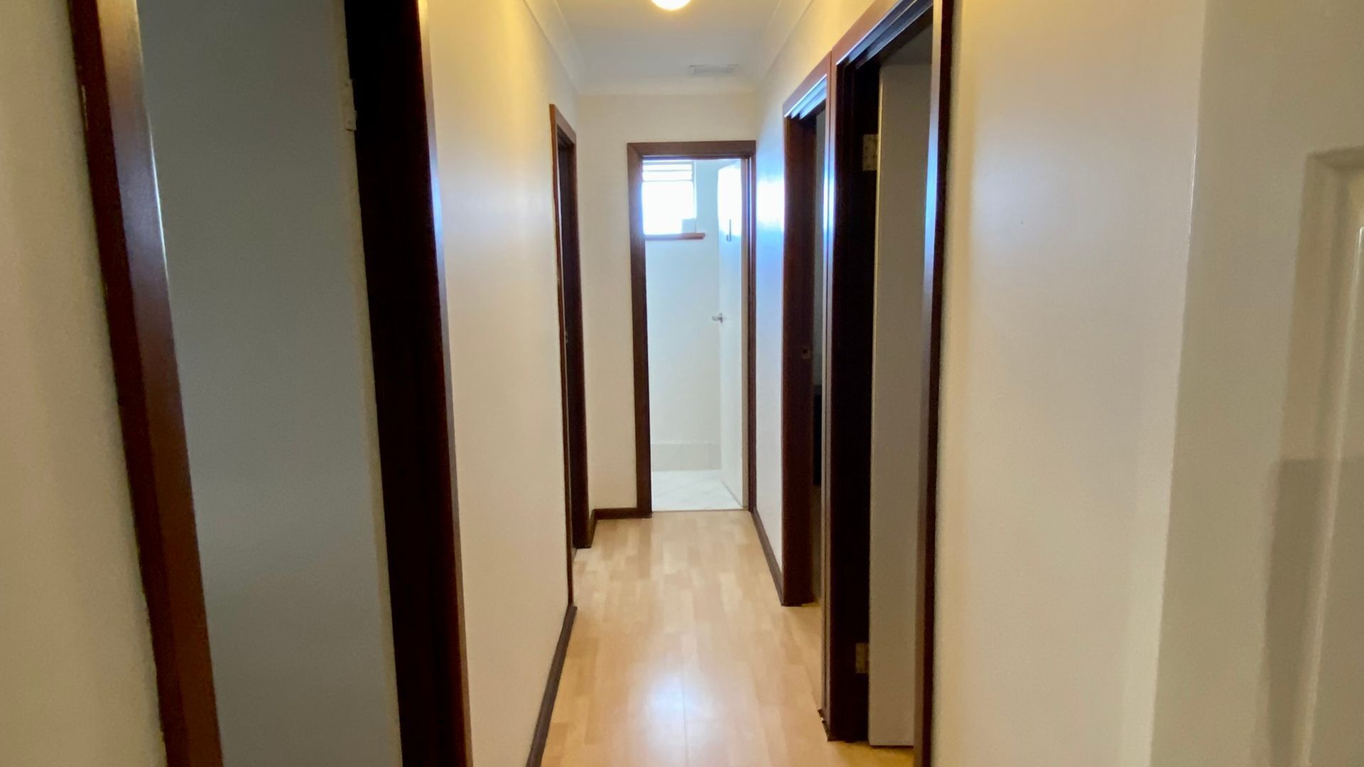 A narrow hallway with wooden doors and a light-colored floor.