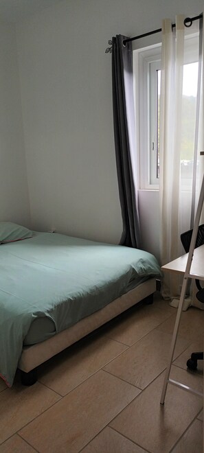A small, single-bed room with a window, a desk, and a chair.