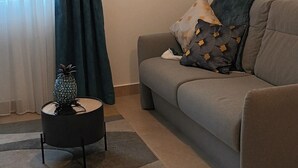 Un salon avec un canapé gris, une table basse ronde, un ananas décoratif et un luminaire suspendu.