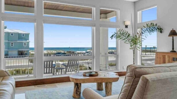 Ett rymligt vardagsrum med stora fönster som vetter mot en strand och erbjuder en vacker utsikt över havet.