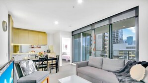 Een modern appartement met een eethoek, een woonkamer met een bank en een salontafel, en een groot raam met uitzicht over de stad.
