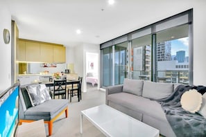 Een modern appartement met een eethoek, een woonkamer met een bank en een salontafel, en een groot raam met uitzicht over de stad.