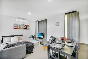 Een moderne hotelkamer met een bed, een bureau, een eettafel gedekt voor twee personen en een televisie.
