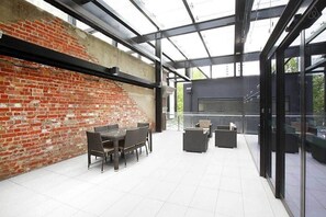 A modern outdoor patio with a brick wall, a glass-enclosed area, and outdoor furniture. - Comfy 2BR Apt Near Southern Cross with City Views (Melbourne)