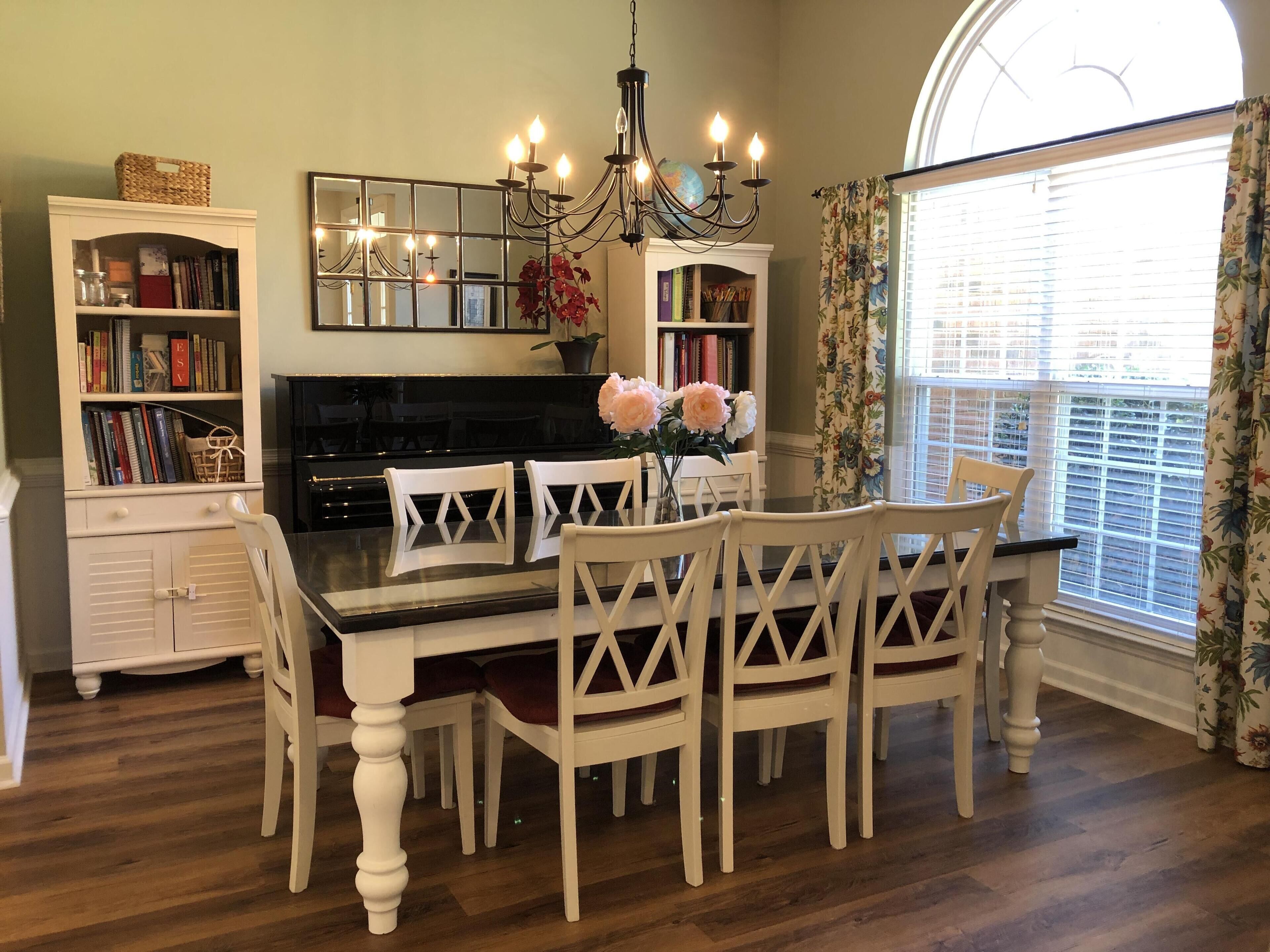A dining area with a glass-top table, white chairs, a chandelier, and bookshelves.