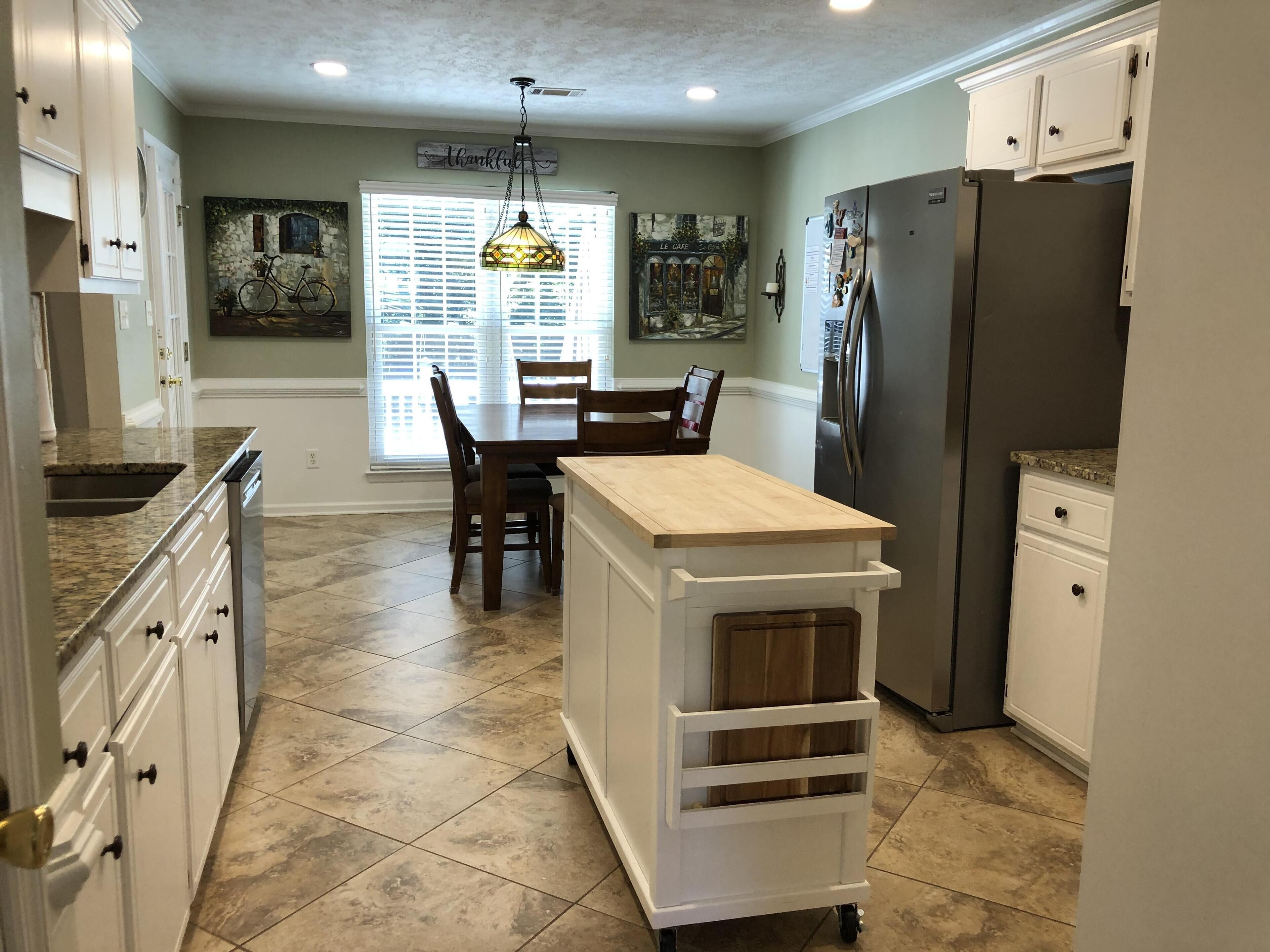 A kitchen with white cabinets, a wooden island, a dining table with chairs, and a refrigerator.
