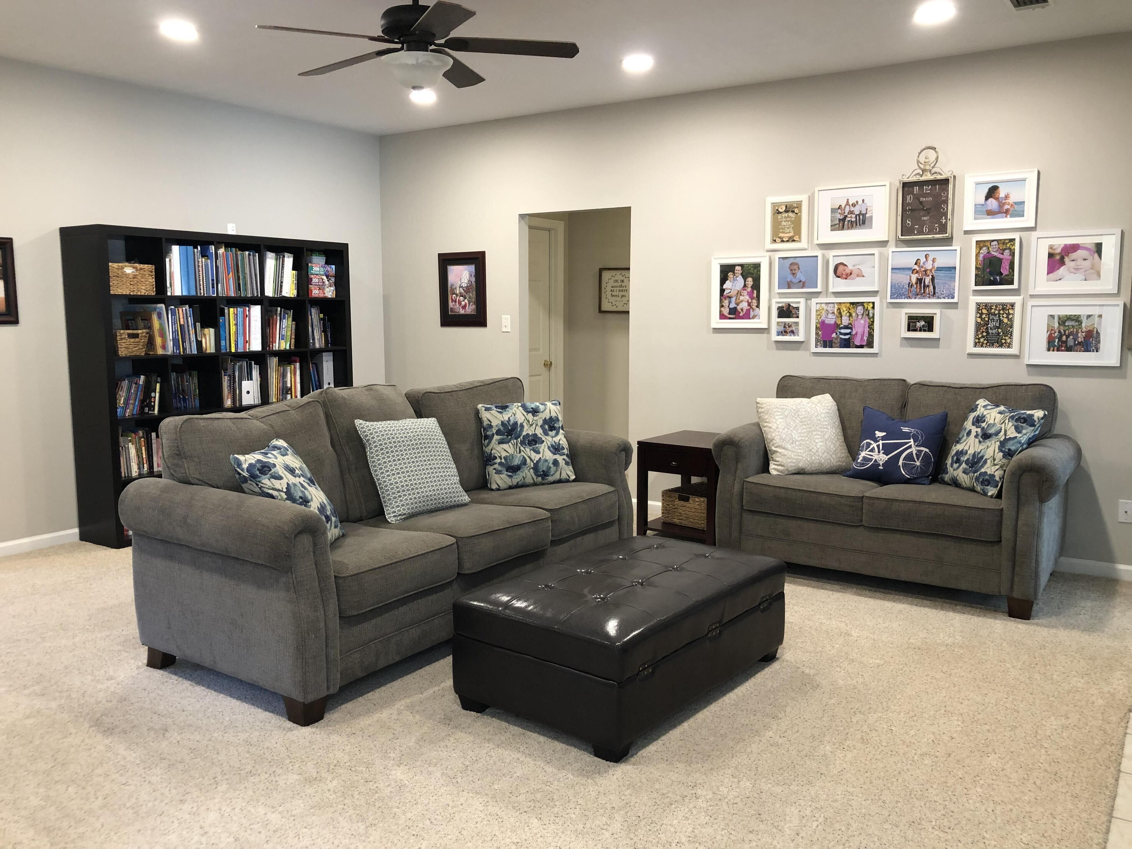 A living room with two grey sofas, a black ottoman, and a bookshelf.