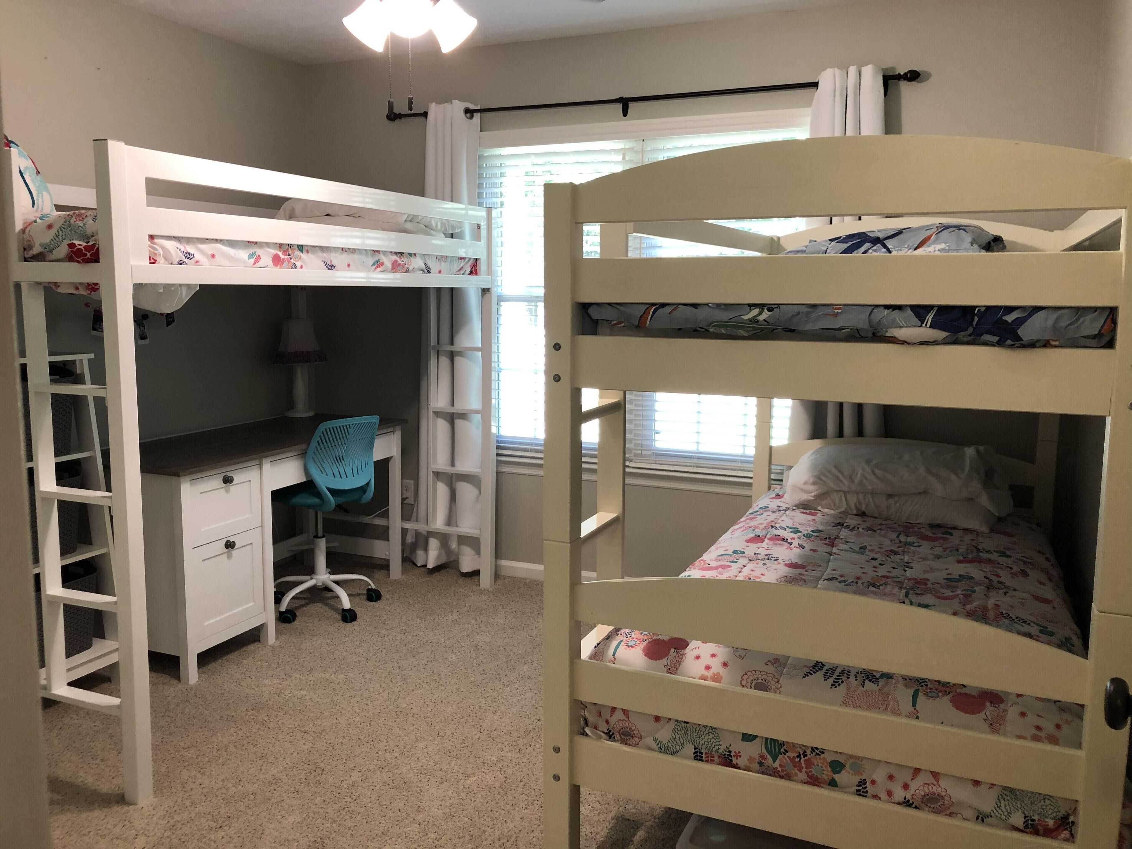 Habitación con literas, un escritorio, una silla, una ventana con cortinas y un ventilador de techo.