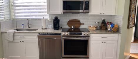 A modern kitchen with white cabinets, stainless steel appliances, a microwave, coffee maker, and a wooden cutting board.