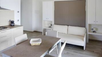 Een compacte kamer met een kitchenette, een slaapbank, een eettafel en een klein kastje.
