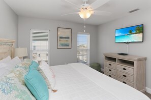 Ein Schlafzimmer mit Bett, Deckenventilator, Fernseher und einem Fenster mit Jalousien.
