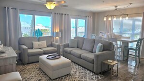 A modern living room with a sofa set, ottoman, and a dining area with a table and chairs.