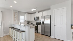 A modern kitchen with white cabinets, stainless steel appliances, and wooden bar stools.