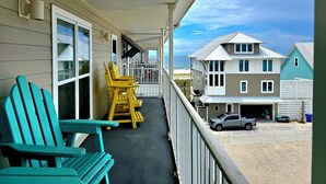A covered porch with chairs, a view of a beach, and a two-story house with a garage.