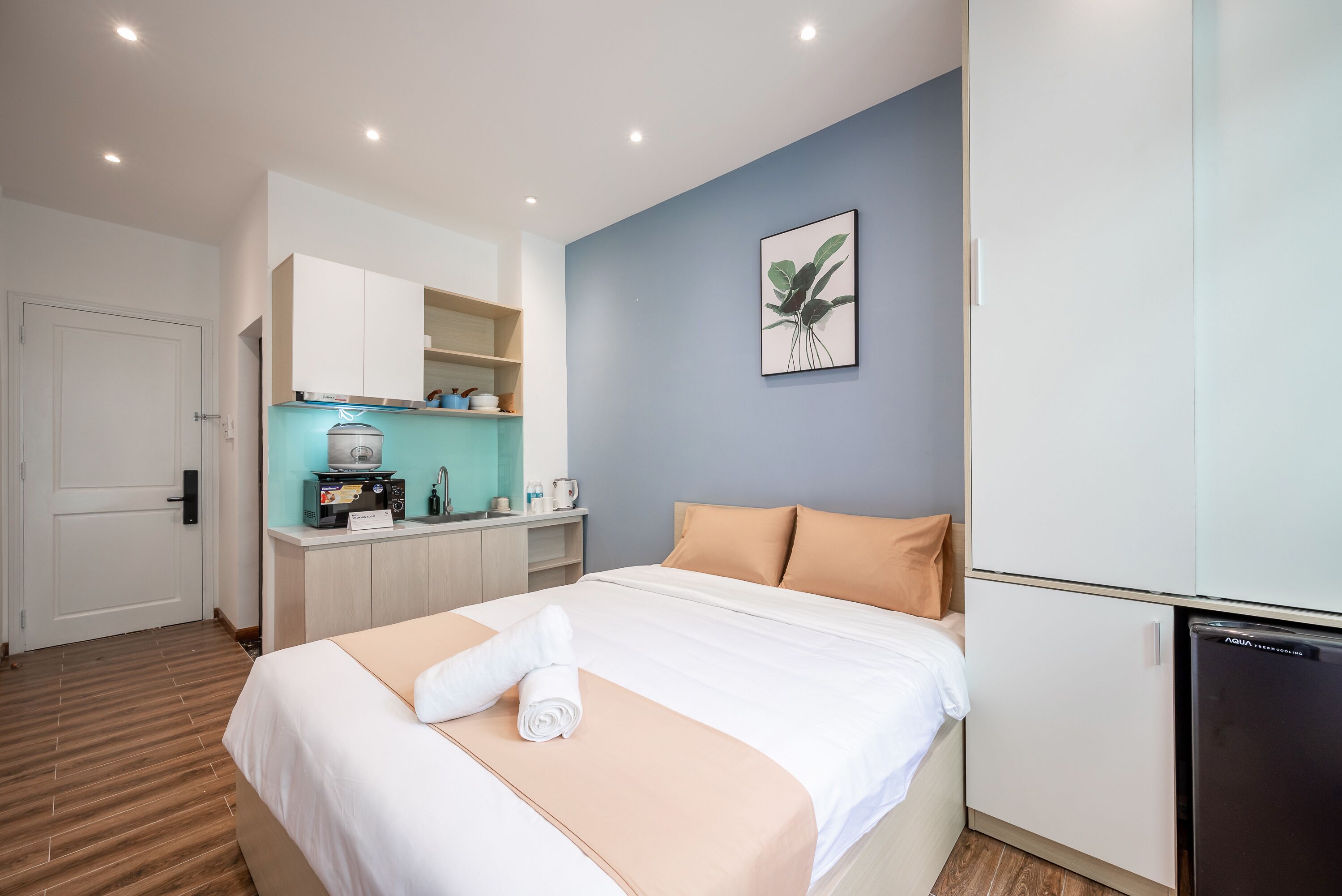Une chambre d’hôtel comprenant un lit, une kitchenette, une porte et une œuvre d’art accrochée au mur.