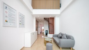 Un espace de vie moderne avec un canapé gris, une petite table ronde et un pouf gris. Un escalier mène à un niveau supérieur.