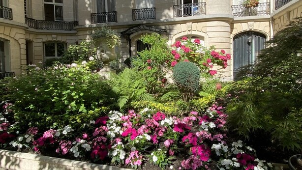 Een meerlaags gebouw met balkons, een tuin met roze en witte bloemen en een stenen gevel.