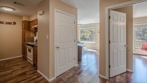 Un pasillo con suelo de madera, paredes color beige y puertas blancas que dan a un balcón.