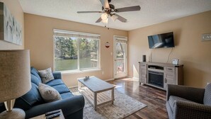 Una sala de estar con ventilador de techo, televisor, sofá, mesa de centro y chimenea.