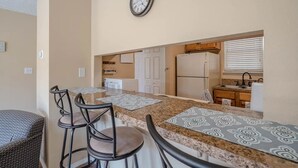 Una cocina compacta con encimera de granito, un refrigerador y un reloj en la pared.