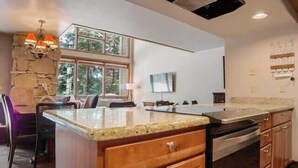 A modern kitchen with granite countertops, wooden cabinets, a built-in oven, and a stone accent wall.