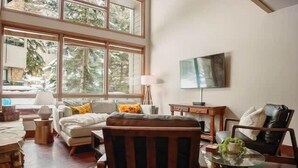 A spacious living room with a large window, a sofa, a coffee table, and a television mounted on the wall.