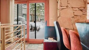 A room with a stone wall, a wooden chair, a bench, and a view through a glass door.
