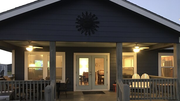 En overdækket veranda med træterrasse, grill og spiseplads med stole og bord.