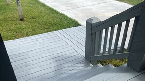 En træterrasse med gråt gelænder, en sti af beton og en græsplæne i baggrunden.