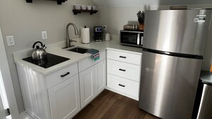 A compact kitchen with white cabinets, a stainless steel refrigerator, a microwave, and a kettle on the stove.