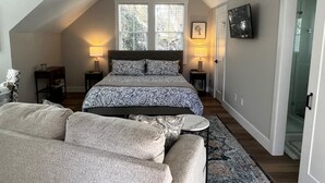 A bedroom with a bed, two bedside lamps, a ceiling fan, a TV on the wall, and a window with blinds.