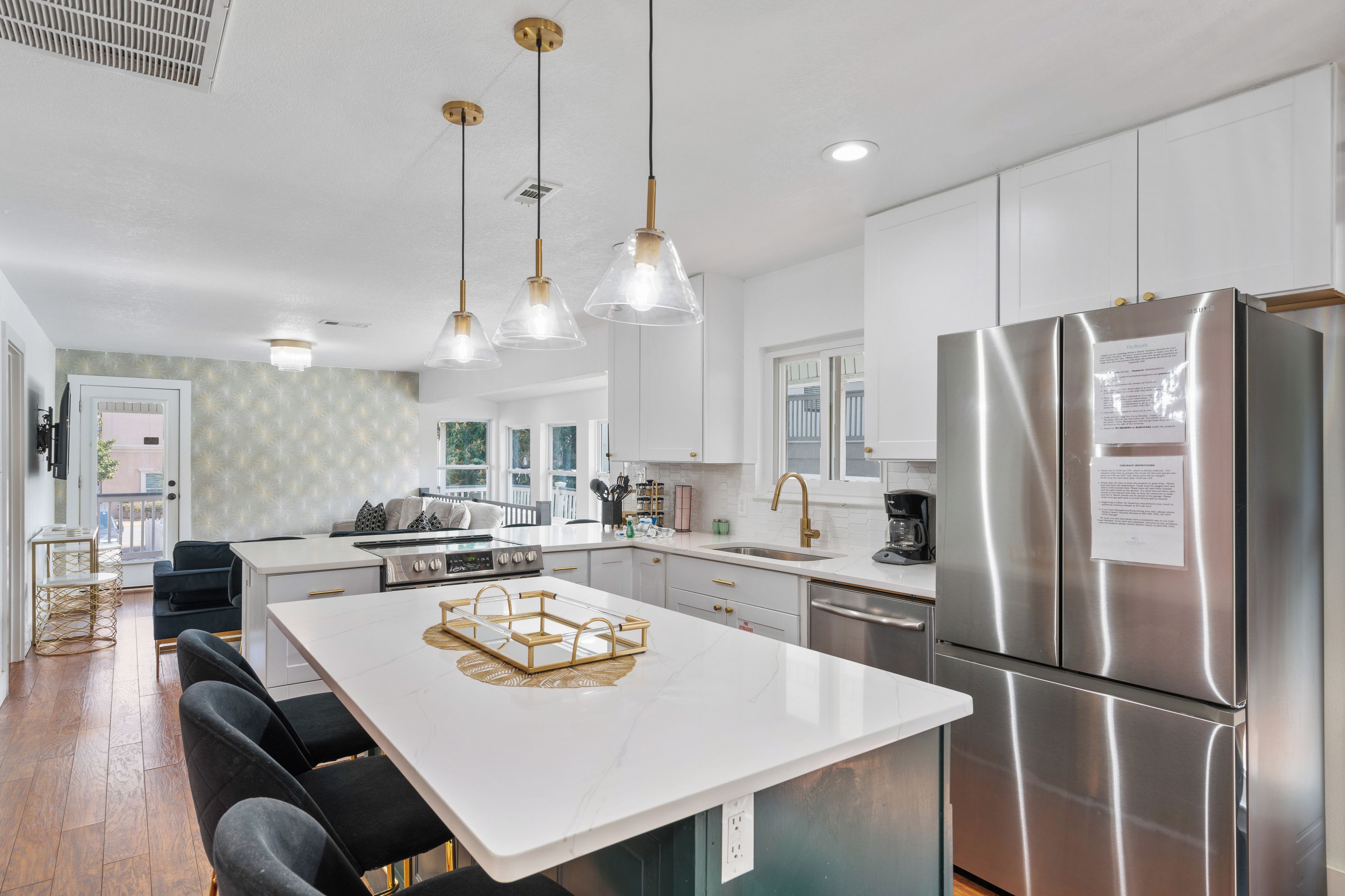 A modern kitchen with a large island, stainless steel appliances, pendant lighting, and a view of the outdoors.