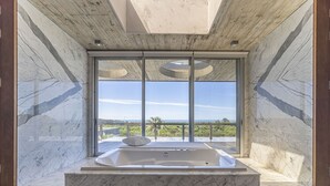 A modern bathroom with a marble floor, a large bathtub, and a view of the outdoors through floor-to-ceiling windows. - Luxury 10,000 sq ft modern house with breathtaking ocean views and every amenity (José Ignacio)