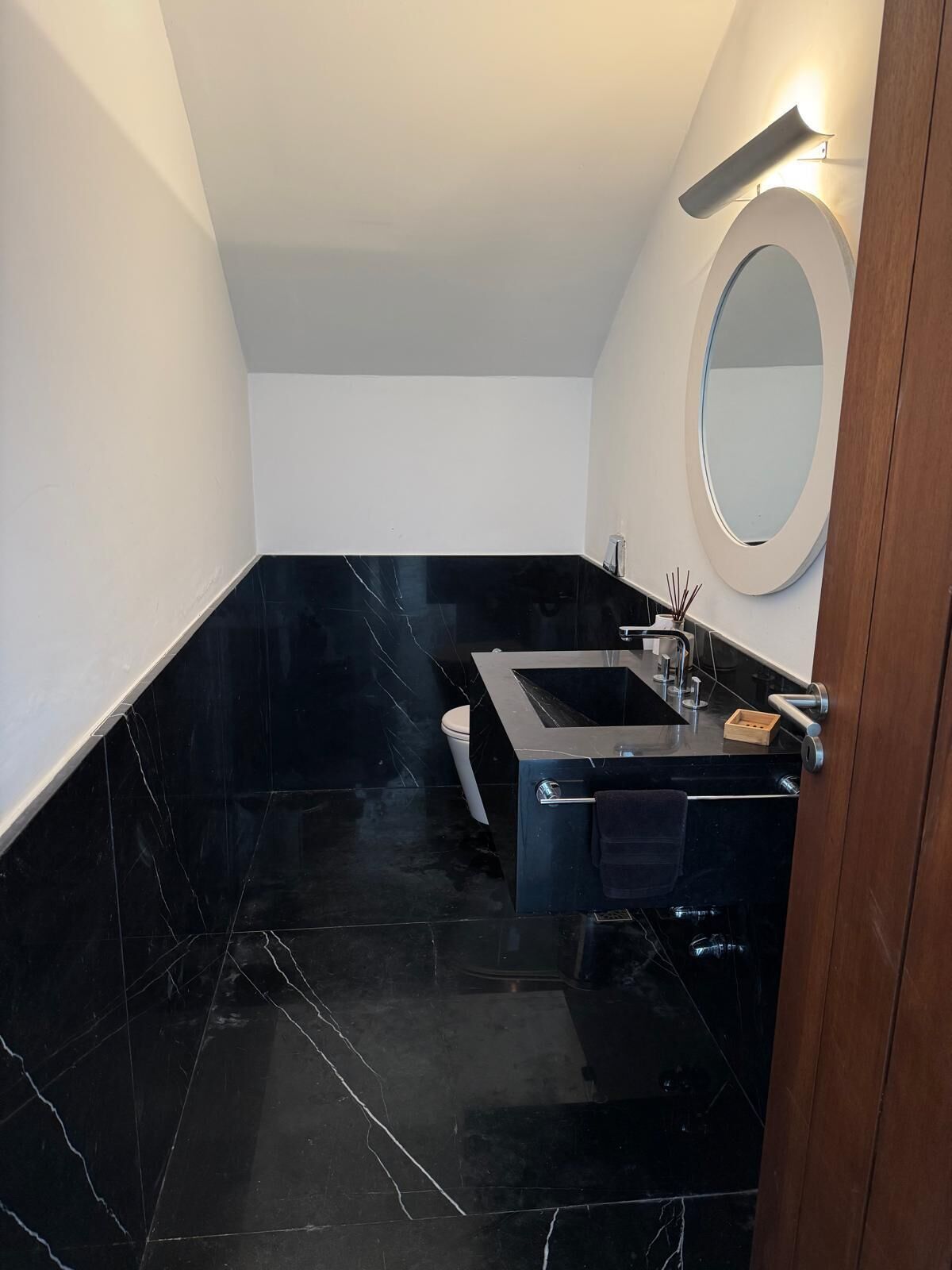 Une salle de bain moderne avec un sol en marbre noir, un grand miroir ovale et un lavabo noir au design épuré.